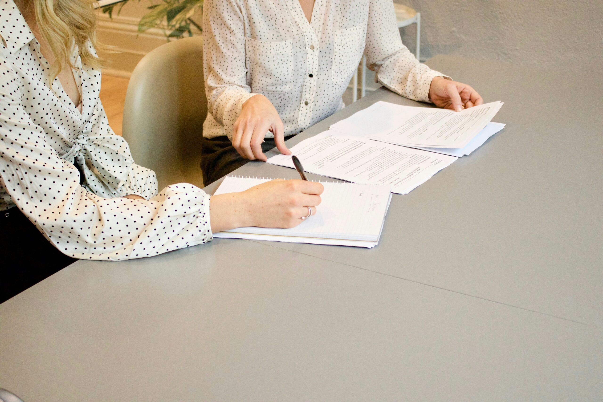 Two women in shirts writing over a couple pieces of paper.