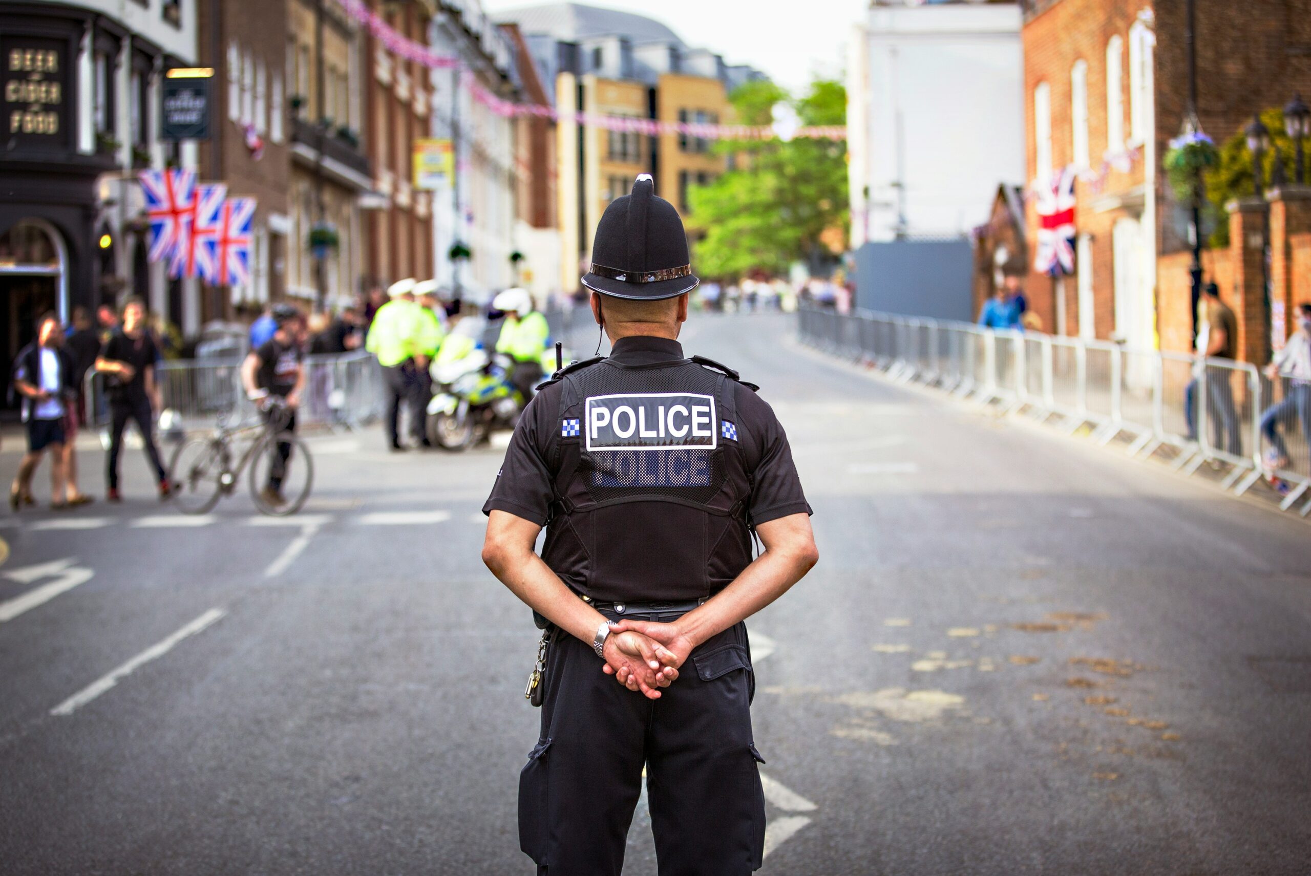 Police officer standing with his arms behind his back in the middle of a built up street